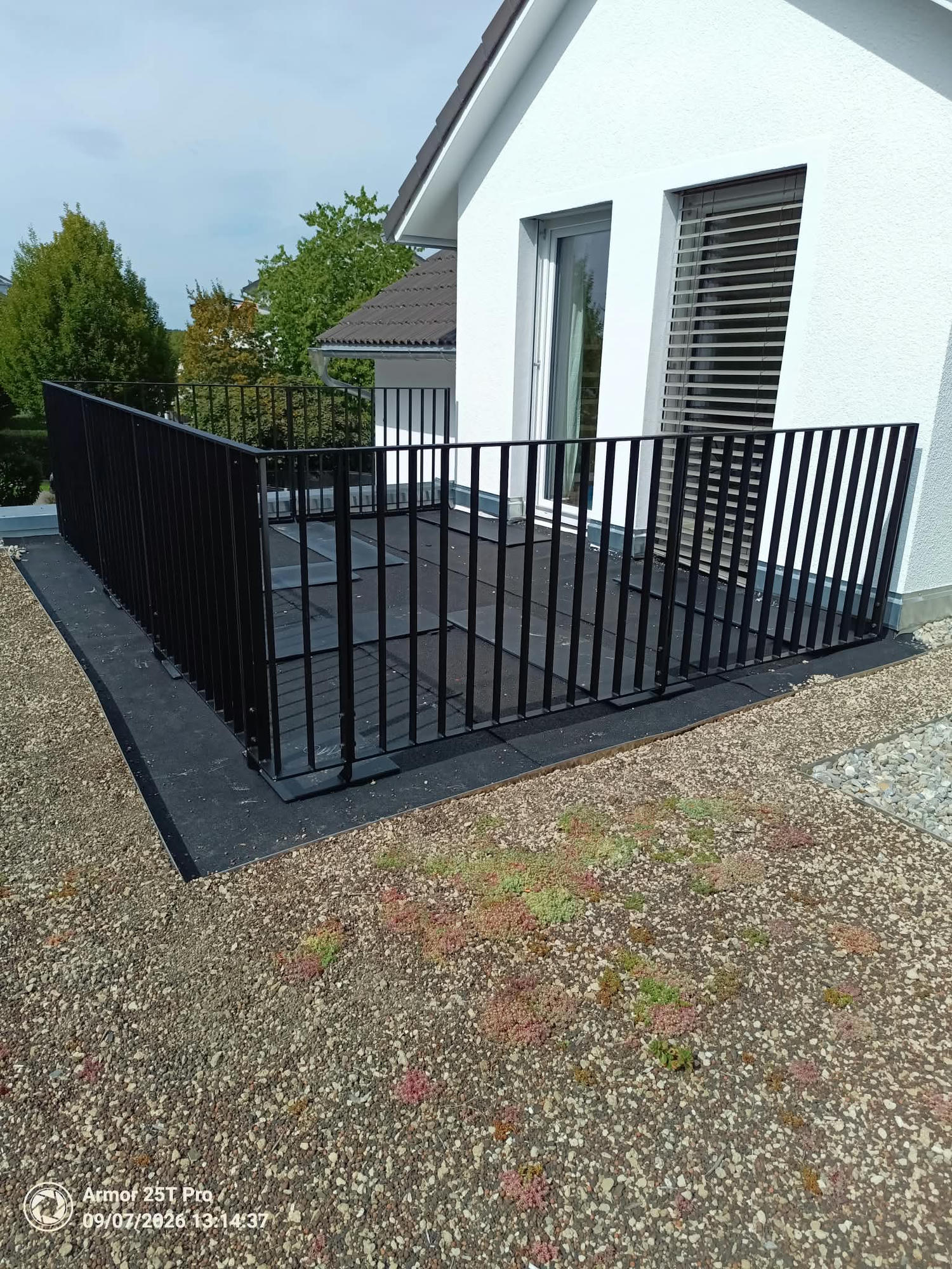 Geländer mit Stäben · GS60 — Schwarzes Balkongeländer mit senkrechten Stäben auf einer Dachterrasse an einem weißen Haus